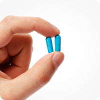 Conceive Plus Men's Fertility Support (FR) two capsules held between fingers, showcasing two bright blue capsules from French-Dutch labelled supplement for male reproductive health; ideal visual detail for dosage and capsule size reference.