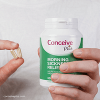 Person holding a bottle of Conceive Plus morning sickness relief supplement with two capsules.