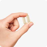 For Conceive Plus Ovulation Pack - Fertility + Ovulation Support (FR), showing a close-up of a hand holding two beige women ovulation support capsules, highlighting their vegetarian shell and compact size, ideal for daily hormonal balance and cycle regulation in women.