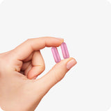 For Conceive Plus Ovulation Pack - Fertility + Ovulation Support (FR), with a close-up of a hand holding two pink women fertility support capsules, highlighting compact, easy-to-swallow size and smooth vegetarian coating designed for women’s daily reproductive health supplementation.