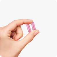 For Conceive Plus Ovulation Pack - Fertility + Ovulation Support (FR), with a close-up of a hand holding two pink women fertility support capsules, highlighting compact, easy-to-swallow size and smooth vegetarian coating designed for women’s daily reproductive health supplementation.